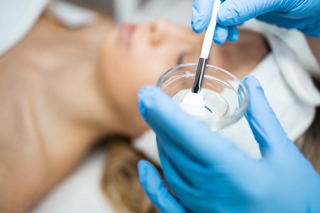 Esthetician dipping a brush into a container with a facial chemical peel gel.