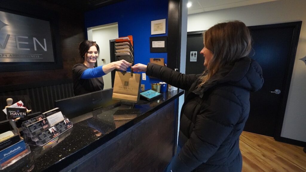 Customer smiling while receiving a branded paper bag after redeeming a wellness gift card.