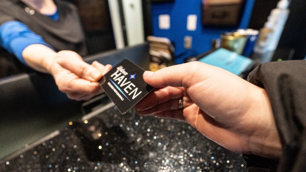 Customer happily presenting an Uptown Haven wellness gift card to a spa receptionist, ready to book a relaxing service.