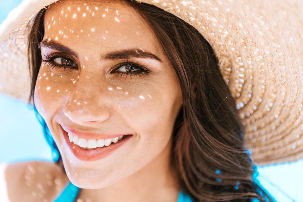 brunette woman in straw hat smiling at camera post carboxy therapy