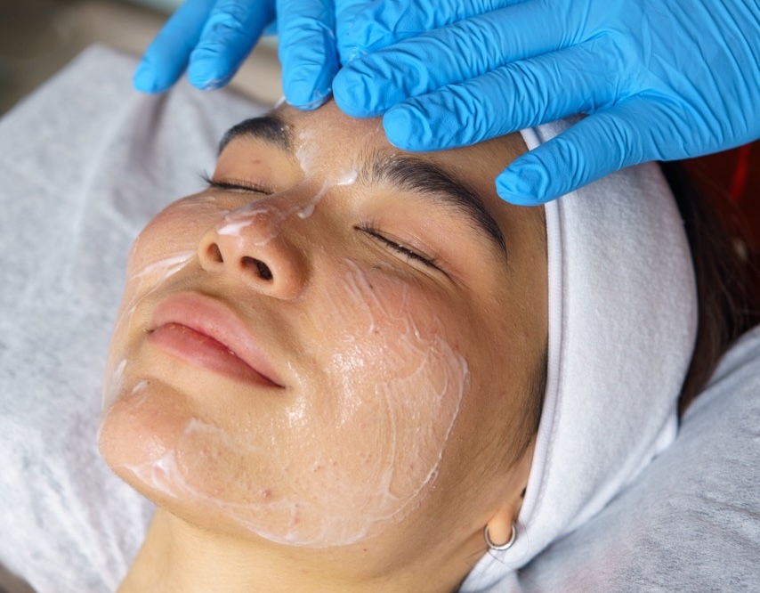 Beautician applying cleansing foam preparing patient's face for professional skincare treatment
