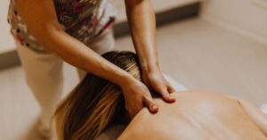 Close-up of a massage therapist applying gentle pressure to a woman's upper back and shoulder area in a warm, dimly lit spa setting.