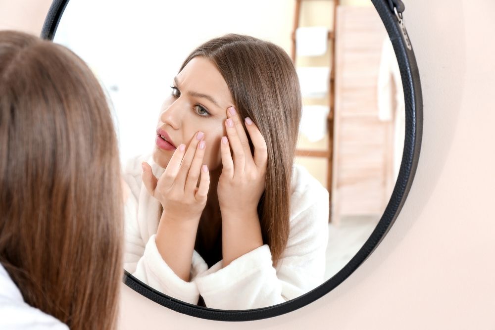 Woman checking her reflection, needing a lash lift and brow lamination for low-maintenance beauty.